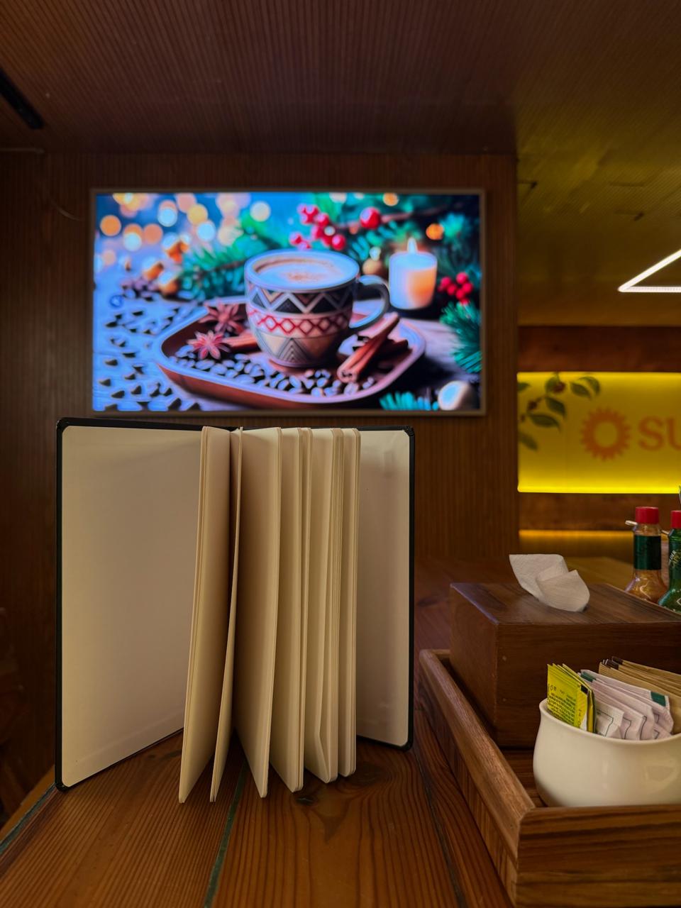 Restaurant setting with a TV screen displaying a festive scene, a book, and a small table with condiments.